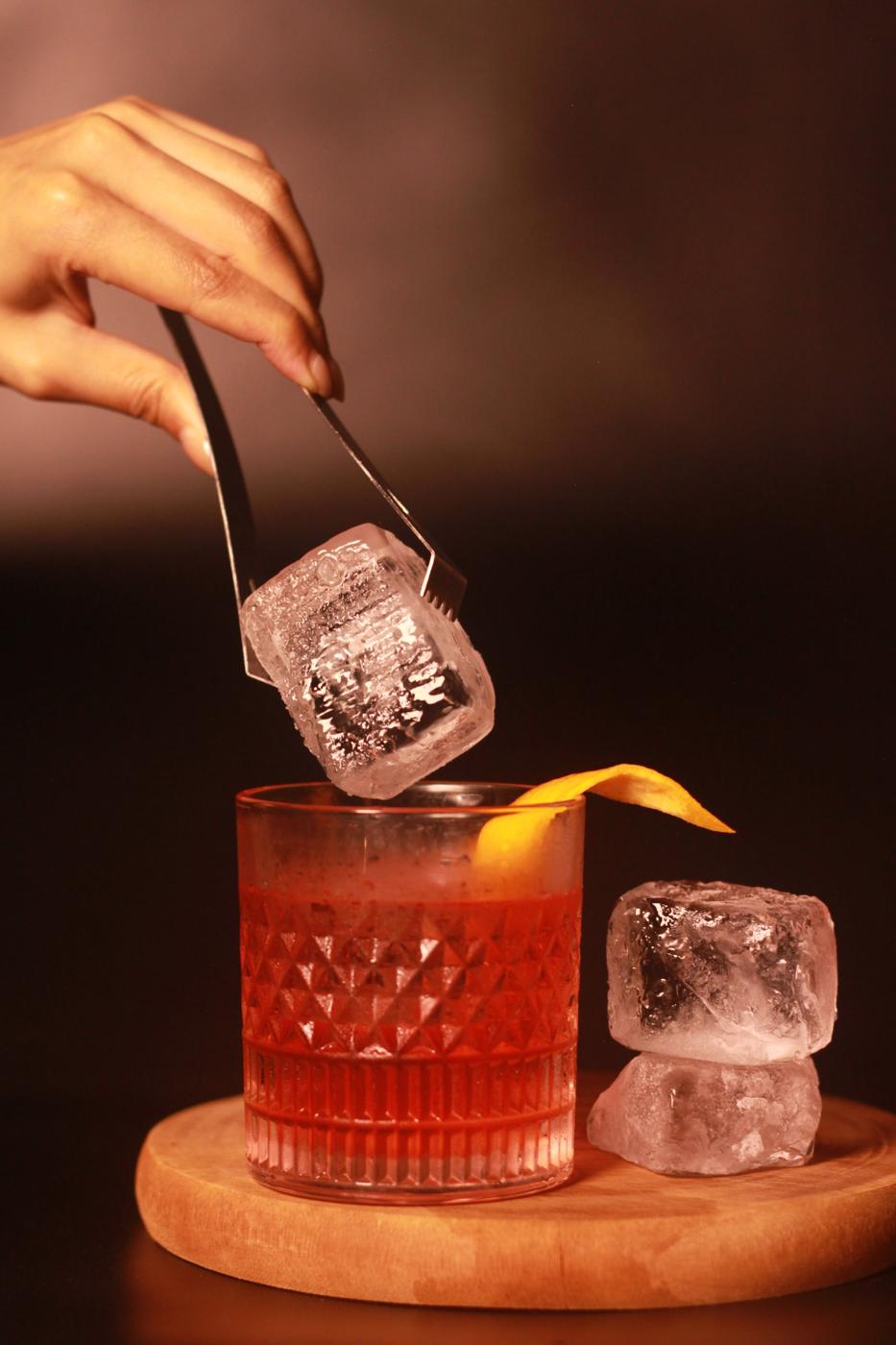Bartender placing a clear ice block into a cocktail
