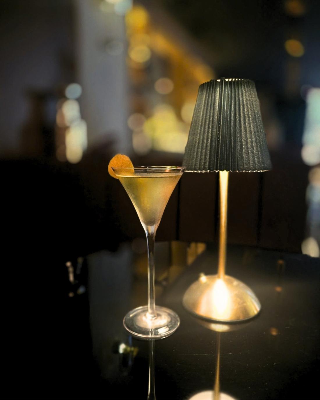 Martini with a citrus twist beside a table lamp