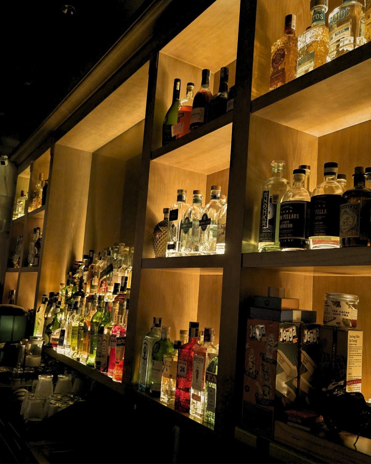 Back bar shelves lit in warm light, lined with gin, tequila and whiskey bottles at The 6ix Saigon